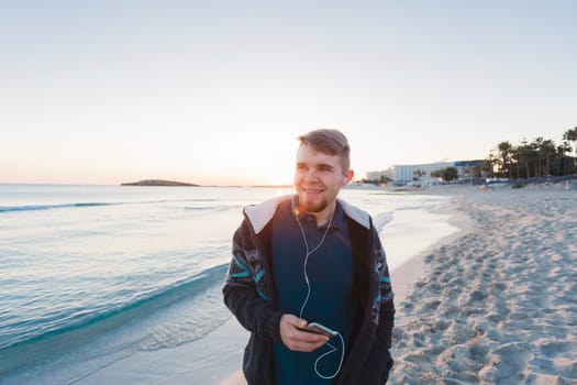 Happy man walking on the beach while listening music with earphones