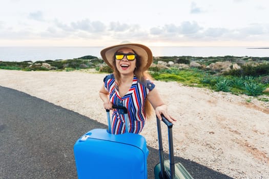 Travel, holiday, summer and vacation concept - Young woman is standing and laughing on road with suitcases.