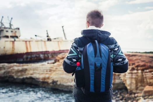 Male tourist looking at an abandoned ship on the sea or ocean. Adventure and tourism concept