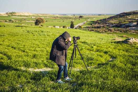 A photographer or traveller using a professional DSLR camera on a tripod in the nature for background