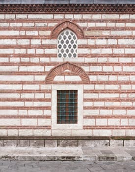 External wall of 16th century Selman Aga Mosque in Uskudar, Istanbul, Turkey. The wall is made of red brick and has arched perforated stucco and wrought iron windows