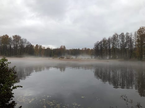 white fog flies over the river, trees are reflected in the water, cloudy, autumn landscape