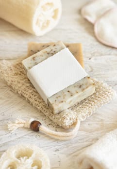 Organic handmade beige soap bar with blank label on soap saver bag near hygiene Items - natural sponges and brush, bamboo toothbrushes and cotton swabs, close up, mockup