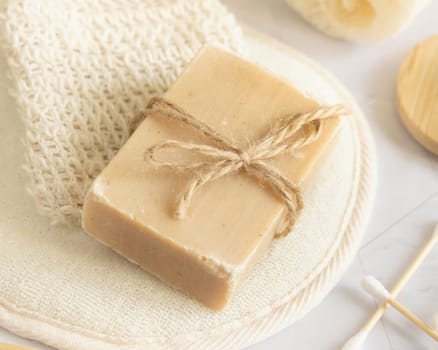 Beige handmade soap bar on sisal soap saver bag on white marble table close up, copy space. Natural herbal products for face and body care
