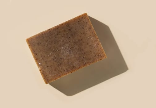 Natural herbal brown soap bar on light beige top view, hard shadows. Hygiene products for Spa and skin care. Using organic handmade soap for everyday bathroom routine