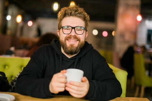 Bearded curly man smiling confident drinking coffee in restaurant or coffee shop. Millennial generation and Gen Y.