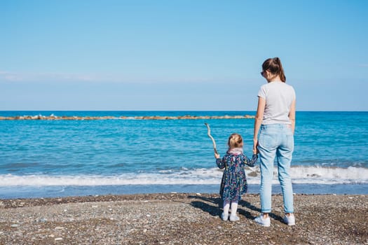 Back view of mother and her little daughter looking at the sea