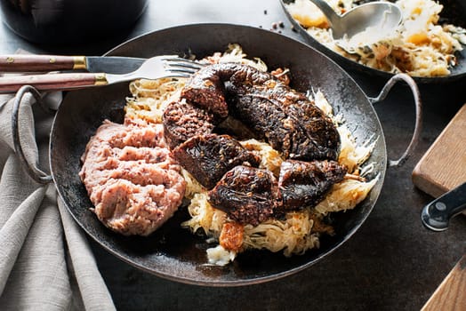 Bloody sausage morcilla, stewed sauerkraut and mashed potato with beans close up. Traditional Slovenian dish with roasted bloody sausage