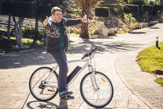 Young man riding bike in park showing thumb up.