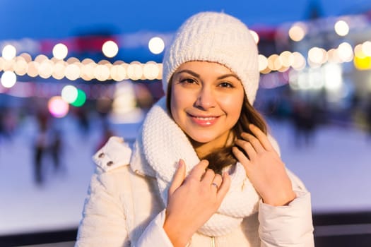 A woman on the rink is skating and taking selfie on smartphone. New Years Eve and Christmas. Fairy lights. Ice and snow mood concept. Winter