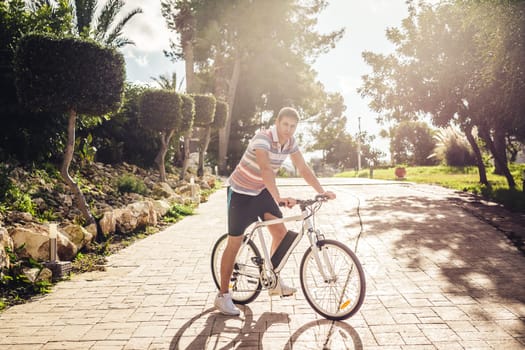 Ready to ride. Handsome young man on bicycle looking at camera and smiling while standing outdoors.