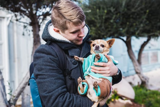 Closeup of handsome young man holding a cute chihuahua dog outdoor.