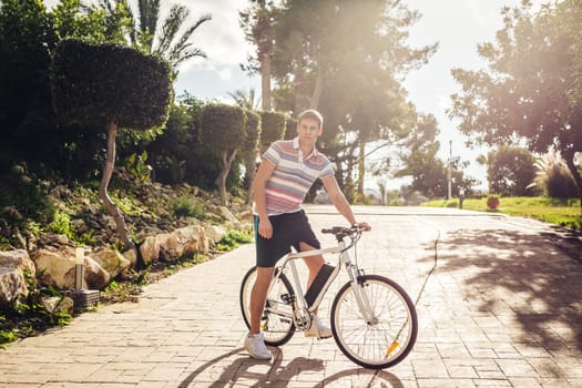 Ready to ride. Handsome young man on bicycle looking at camera and smiling while standing outdoors.