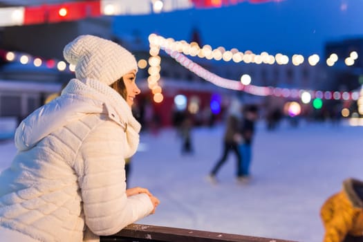 A woman on the rink is skating and taking selfie on smartphone. New Years Eve and Christmas. Fairy lights. Ice and snow mood concept. Winter