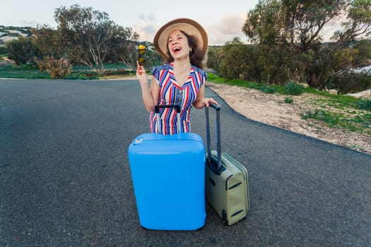 Happy laughing young woman with suitcases on the road