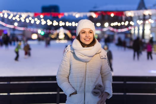A woman on the rink is skating and taking selfie on smartphone. New Years Eve and Christmas. Fairy lights. Ice and snow mood concept. Winter