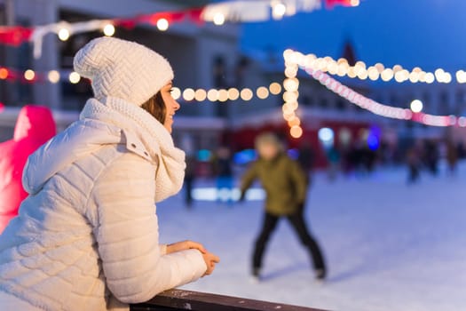 Christmas, winter, technology and leisure concept - happy young woman taking picture with smartphone on ice skating rink.