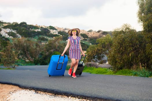 Happy smiling woman with blue suitcase on a road.
