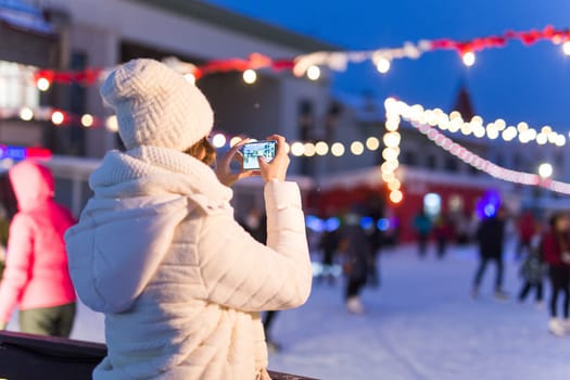 Happy young woman in winter on the ice rink taking picture on smartphone.