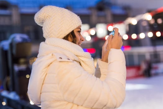 Happy young woman in winter on the ice rink taking picture on smartphone.