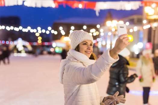 Happy young woman in winter on the ice rink taking picture on smartphone.