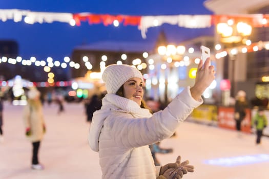 Happy young woman in winter on the ice rink taking picture on smartphone.