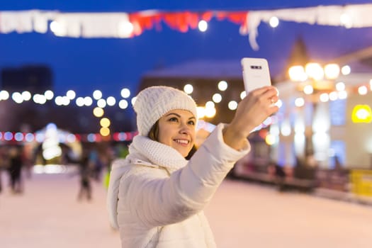 Happy young woman in winter on the ice rink taking picture on smartphone.