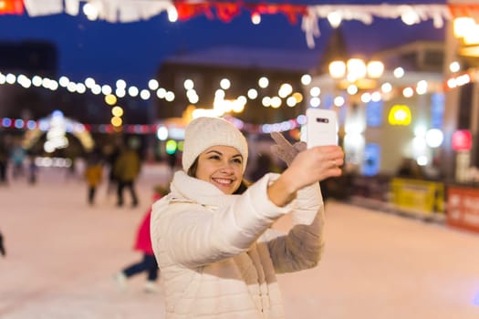 Happy young woman in winter on the ice rink taking picture on smartphone.