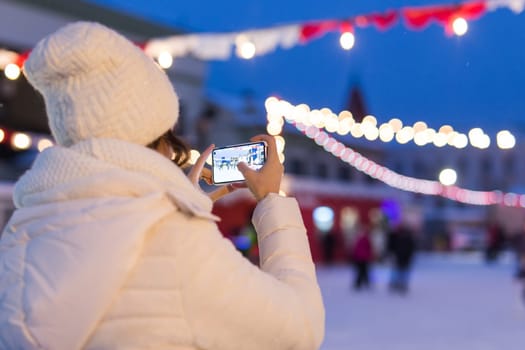 Happy young woman in winter on the ice rink taking picture on smartphone