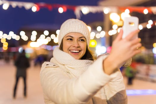 Happy young woman in winter on the ice rink taking picture on smartphone.