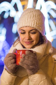 Christmas holidays. Beautiful smiling woman in warm clothing with cup of hot coffee outdoor in winter