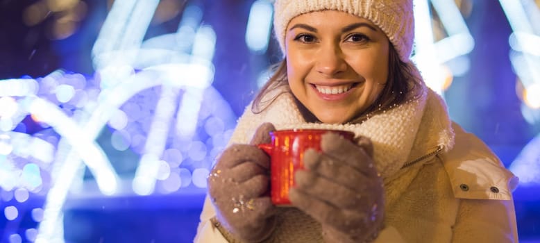 Christmas holidays. Beautiful smiling woman in warm clothing with cup of hot coffee outdoor in winter