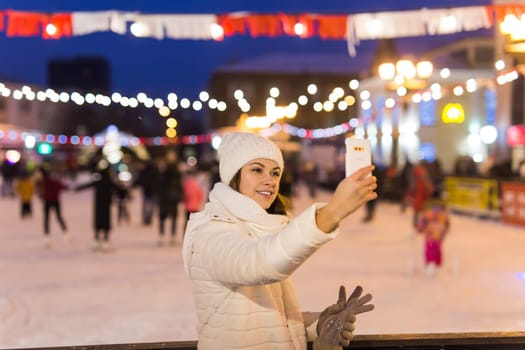 Happy young woman in winter on the ice rink taking picture on smartphone.