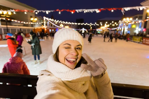 Christmas, winter, technology and leisure concept - happy young woman taking picture with smartphone on ice skating rink.