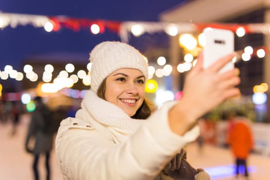 Happy young woman in winter on the ice rink taking picture on smartphone.