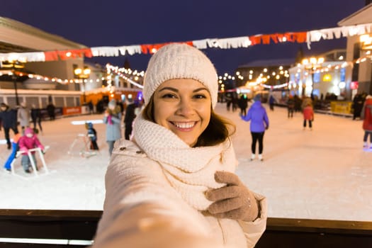 Happy young woman in winter on the ice rink taking picture on smartphone.