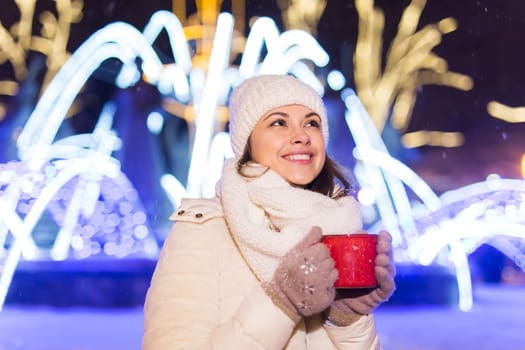 Christmas holidays. Beautiful smiling woman in warm clothing with cup of hot coffee outdoor in winter