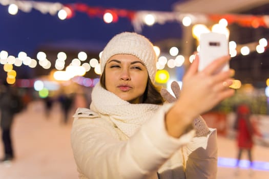 Happy young woman in winter on the ice rink taking picture on smartphone.
