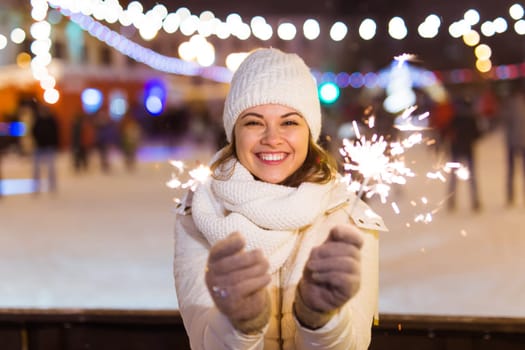 Girl holding a sparkler in her hand. Outdoor winter city background, snow, snowflakes