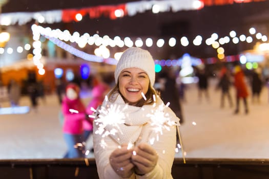 Young beautiful woman in knitted hat and scarf standing in the city with bengal light, sparkler. Concept celebration and christmas
