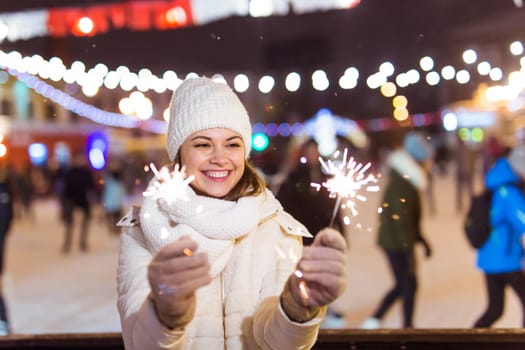 Girl holding a sparkler in her hand. Outdoor winter city background, snow, snowflakes
