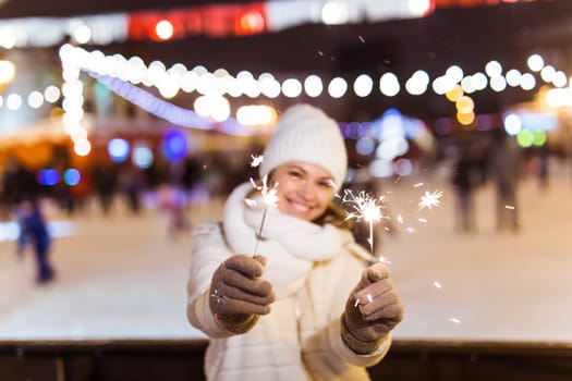 Girl holding a sparkler in her hand. Outdoor winter city background, snow, snowflakes