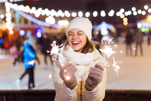 Young beautiful woman in knitted hat and scarf standing in the city with bengal light, sparkler. Concept celebration and christmas