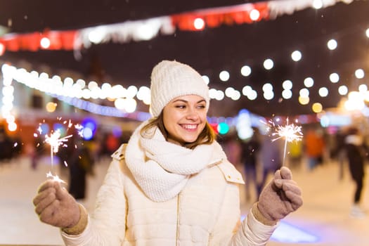 Young beautiful woman in knitted hat and scarf standing in the city with bengal light, sparkler. Concept celebration and christmas