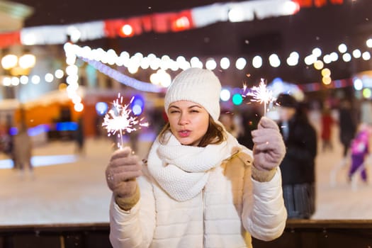Girl holding a sparkler in her hand. Outdoor winter city background, snow, snowflakes