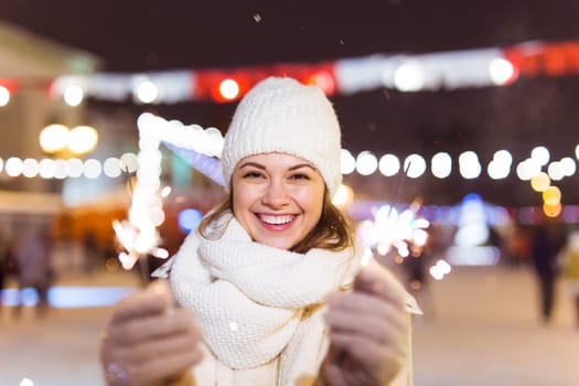 Girl holding a sparkler in her hand. Outdoor winter city background, snow, snowflakes