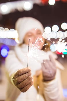 Young beautiful woman in knitted hat and scarf standing in the city with bengal light, sparkler. Concept celebration and christmas