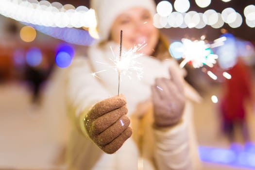 young woman wearing winter knitted clothes holding sparkler outdoors over snow background. Christmas holidays.