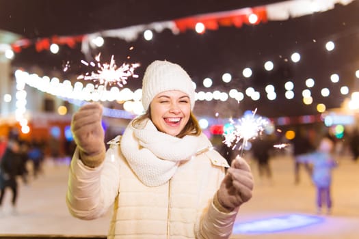 Girl holding a sparkler in her hand. Outdoor winter city background, snow, snowflakes