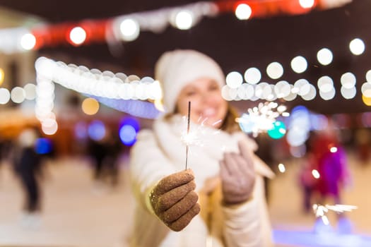 Girl holding a sparkler in her hand. Outdoor winter city background, snow, snowflakes